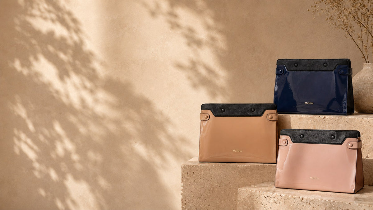 Trois pochettes Maïsha en simili verni caramel, bleu marine et rose disposées sur des marches en pierre travertin, ambiance lumineuse et élégante
